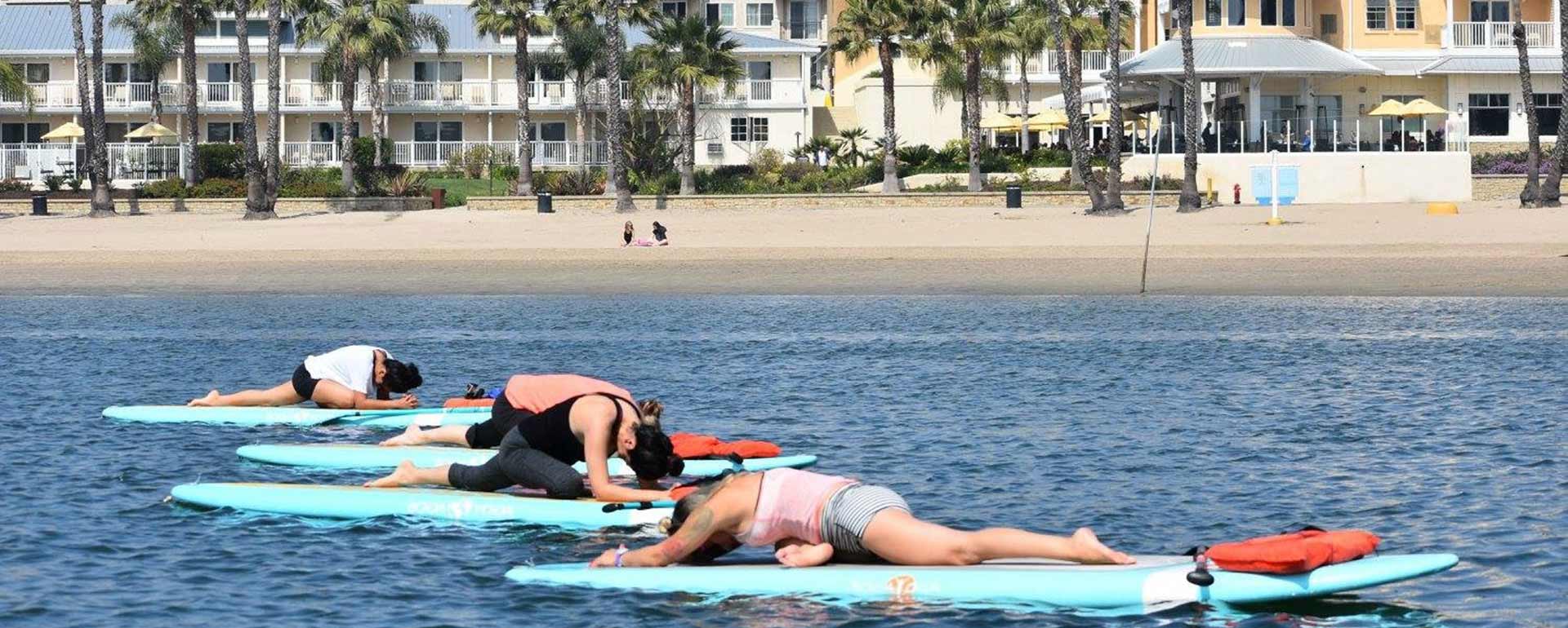 The same class lying back in savasana on their boards, drifting on calm water with the beach behind